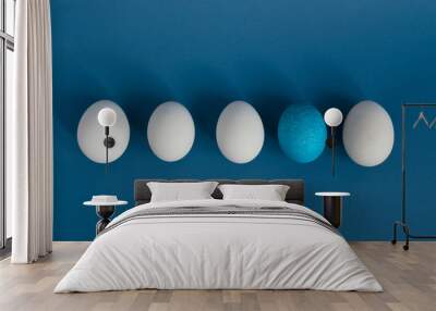 White eggs and blue egg in a row on blue background Wall mural