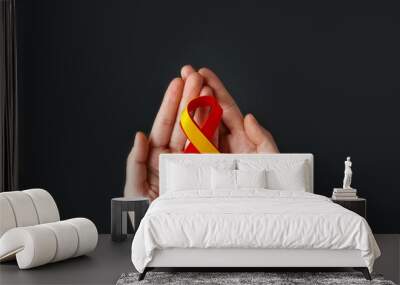 World hepatitis day. Adult hands holding red yellow ribbon on black background. Awareness of prevention and treatment viral hepatitis. Liver cancer. World cancer day. copy space. banner Wall mural