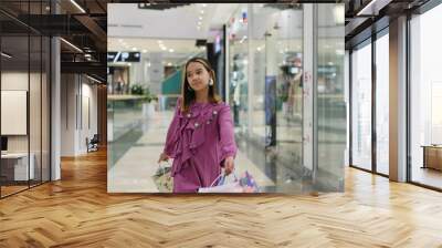 Little fashion girl with packages in a large shopping center. Pretty smiling little girl with shopping bags posing in the shop Wall mural