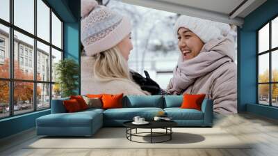 Two lovely women laugh and hug against the background of a snowy winter park. female friendship concept Wall mural