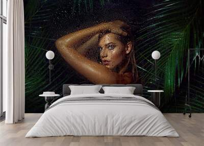 A beautiful, young, tanned girl with wet hair and wet skin is standing in the jungle in the rain. Wall mural