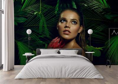 A beautiful tanned girl with natural make-up and wet hair stands in the jungle among exotic plants. Wall mural