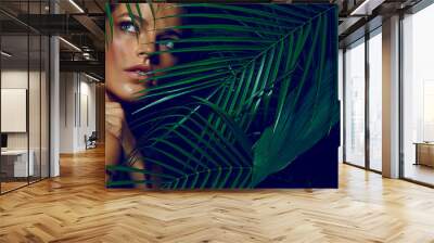 A beautiful tanned girl with natural make-up and wet hair stands in the jungle among exotic plants Wall mural