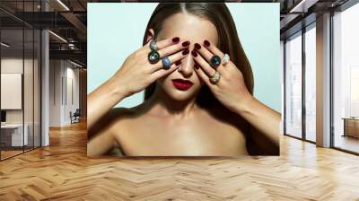 A beautiful young girl with smooth skin and an elegant hairstyle closes her eyes with her hands. Beautiful expensive rings on the fingers. Wall mural