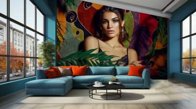 Beautiful sexy dark-skinned young girl posing against the backdrop of a motley colorful wall surrounded by palm leaves. Wall mural