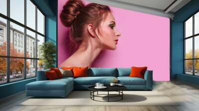 Beautiful young graceful girl with long neck on a pink background in studio. The hair is collected in a high beam. Brown. Fresh bright make-up, green shadows, pink lipstick and blush. Cosmetics.
 Wall mural