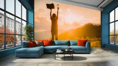 The silhouette of a woman's hand with the symbol of the cross on the sunset background, the cross, symbol of faith It is a belief in Christian concepts. Wall mural