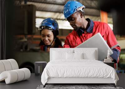 Two engineer heavy Industry Engineers Wearing Safety Uniform and Hard Hats Working on Laptop Computer. African American Technician and Female Worker Talking on a Meeting in a Factory. Wall mural