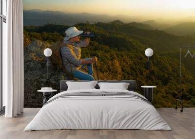 Young man hiker on a top of a mountain standing on top of cliff in summer mountains at sunset and enjoying view of nature Wall mural