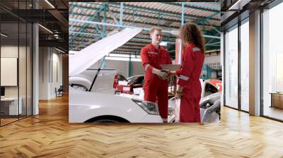 Caucasian male mechanic working in garage, two standing in front of smart car handshake congratulations After fixing the car, a male mechanic wears a red mechanic's uniform. Wall mural