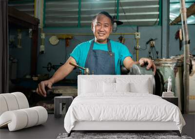 Portrait of an Asian man smiling. Senior craftsman who is skilled in craftsmanship, is controlling, skillfully operating a lathe, is in a small factory that is his family business.. Wall mural