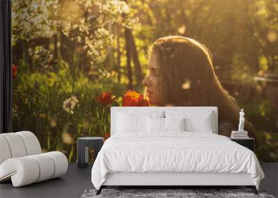 Girl in white dress smelling tulip in sunset among fluff, dandelions and cherry flowers Wall mural