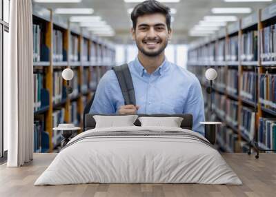 Cheerful Indian student in blue shirt with backpack and a tablet on hand in college library Wall mural