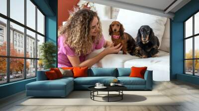 One blond woman wearing pink dress sitting on the floor petting her two Dachshund dogs on the couch in the living room Wall mural