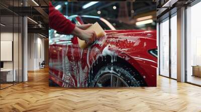 A worker washing a red car using a sponge at a car wash facility. Wall mural