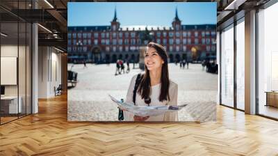 Visiting famous landmarks and places.Cheerful female traveler at famous Plaza Mayor square reading a map. Marid,Spain travel experience. Backpacker, travel photography. Wall mural