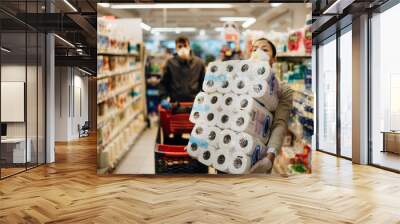 Woman couple with mask and gloves panic buying and hoarding toilette paper in supply store.Pathogen virus pandemic quarantine.Prepper buying bulk cleaning supplies due to Covid-19.Focus on the paper Wall mural