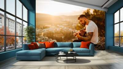 Young guitarist playing acoustic guitar and looking to sunset.Searching inspiration.Music creator.New artist.Musical talent.Handsome guitarist enjoying sunset and playing acoustic guitar. Wall mural