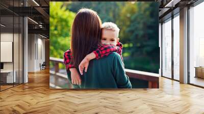 The woman stands with her back and holds the hugging boy's son. A mother hugs a child outdoors in a Park on a summer day. Happy authentic family childhood lifestyle. Wall mural