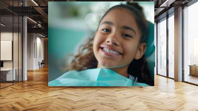 A close up photo of smiling teenager girl in dental braces, sitting in dentist’s chair, orthodontist visit, beautiful teeth in brace system, young African American woman with blue dentist napkin Wall mural