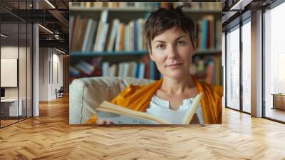 a contemplative woman reading a book with bookshelves behind Wall mural