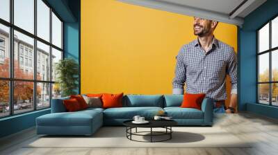 Smiling man in a checkered shirt standing confidently against a yellow background with a copy space Wall mural