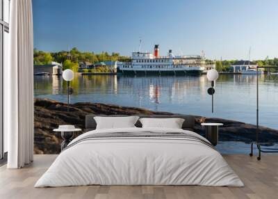 Cruise steam ship moored by the pier at a small tourist town waterfront. Sunny summer day, blue sky. Local tourism and attractions concept. Wall mural