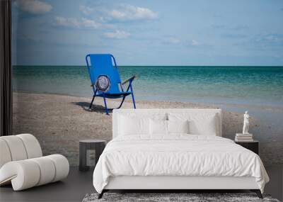 Blue beach chair and stylish white hat on the shore of the blue sea island of sand in the water blue sky white clouds sea wave beautiful landscape summer vacation beach sand weekend rest Wall mural