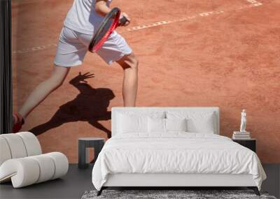 Boy plays tennis on red clay court. Child on tennis court hits forehand. Young tennis player with racket in action. Kids sports background with shadow. Banner size. Copy space Wall mural