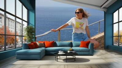 CAPE DE FORMENTOR . SPAIN.A girl in sunglasses sits on the observation deck of Mirador Es Colomer. The wind blows her hair around her face. Majorca. Wall mural