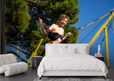 Children have fun jumping on bungee trampoline secured with rubber bands. Sunny day Wall mural