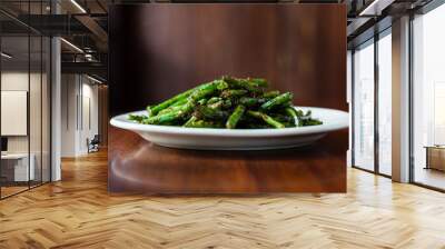 Close up side view of spicy szechuan green beans on white plate and wood surface Wall mural