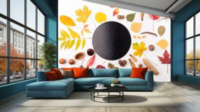 collection of various autumn leaves, nuts, seeds, natural objects arranged around a black circular object in the center. The leaves are in shades of yellow, red, and green, perfectly fall season Wall mural