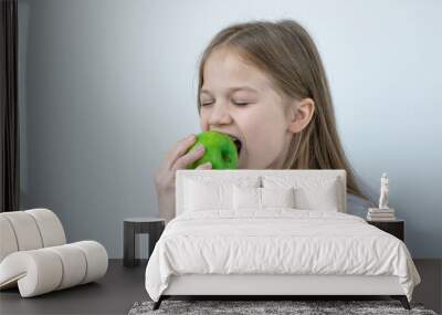 Cute little girl in white T-shirt eating green apple. Health care, fruits, healthy eating, dental care for kids. child bites an apple. Wall mural