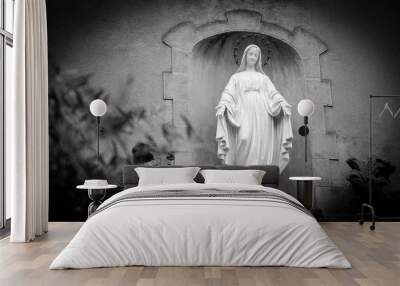 Statue of Madonna with stars nimbus on the front of Cathedral of Notre Dame of Assumption in Entraveaux (France) and olive tree at foreground. Selective focus on the statue. Black and white photo. Wall mural