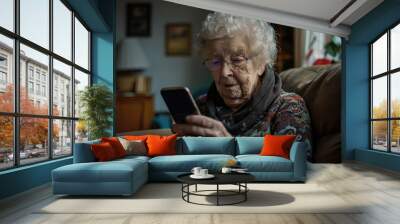 Elderly woman using a smartphone while sitting on a couch at home Wall mural