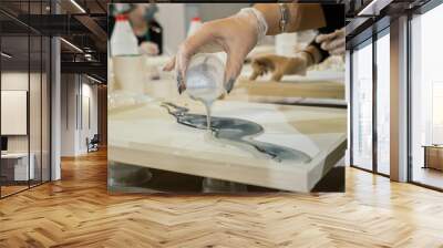 female hand in a transparent glove pours a vivid colored resin on a wooden flat surface Wall mural