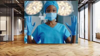 Female surgeon in operating room. African American woman in surgeon scrubs, mask and surgical hat preparing to do surgery, holding up her hands in medical gloves. Doctor in protective wear Wall mural