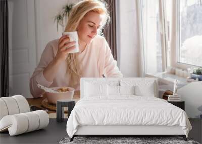 Thoughtful young woman in bathrobe eating breakfast in kitchen Wall mural