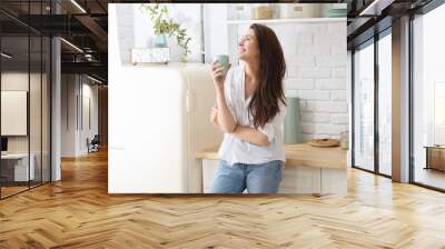 Young happy woman drinking coffee on the kitchen in the morning Wall mural