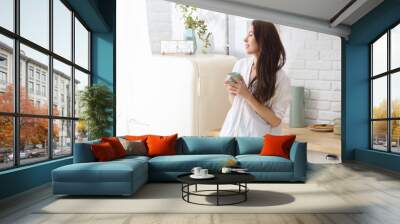 Young happy woman drinking coffee on the kitchen in the morning Wall mural