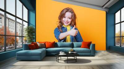 Cute little girl showing thumbs up on orange background Wall mural