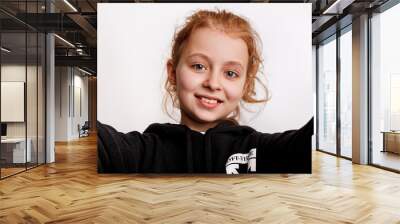 Photo of positive curly redhead kid girl take selfie on white background Wall mural