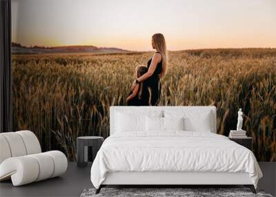 Rear view of mother and her daughter staying in golden wheat field on sunset Wall mural