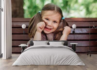 toddler funny girl having fun and sitting on the wooden bench in park Wall mural