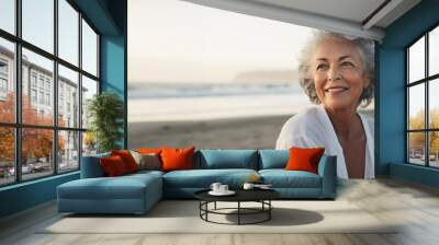 Lifestyle portrait of happy attractive elderly woman sitting on beach at sunset Wall mural