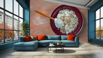 Loose cottage cheese on a shallow brown plate with a wooden spoon with sour cream and seeds, top view Wall mural