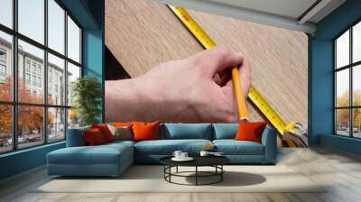 Man's hands measuring wooden plank with a tape line. Wall mural