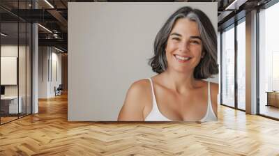 Studio portrait of happy and attractive mature woman with gray hair, smiling and wearing white tank top Wall mural