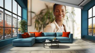 Successful professional mature black woman with short hair wearing tan business suit and standing in office interior with natural window light Wall mural